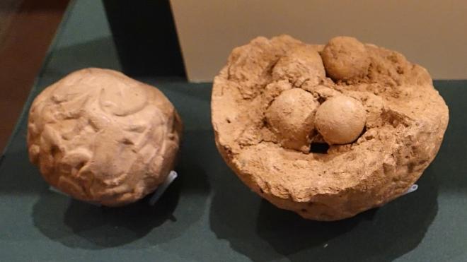 Two clay bullae, one complete and sealed, the other broken with tokens visible.